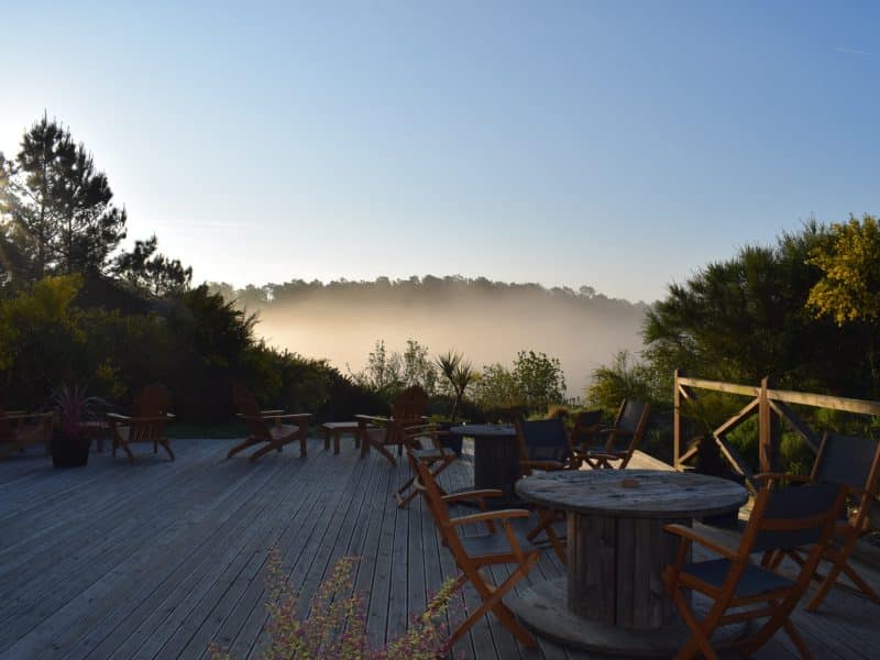 Chalet en bois avec terrasse ensoleillée offrant une vue sur la brume matinale.