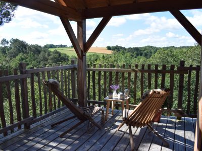 Cabane perchée en Bretagne avec terrasse en bois et vue sur la nature verdoyante.