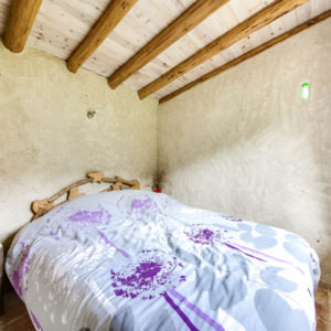 Chambre douillette en cabane, murs en terre et lit confortable décoré de fleurs.