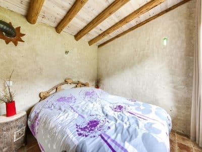 Chambre douillette en cabane, murs en terre et lit confortable décoré de fleurs.
