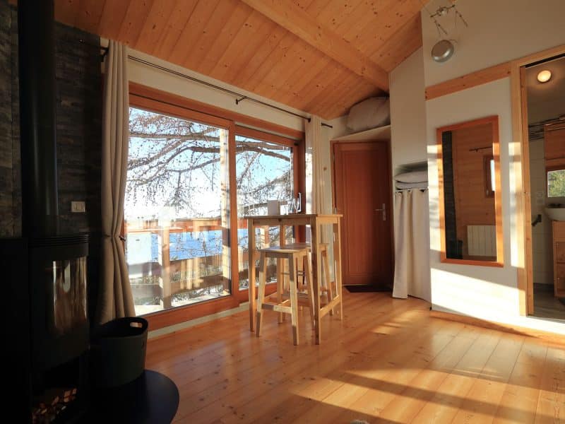 Cabane en bois lumineuse avec vue sur le lac et poêle à bois chaleureux.