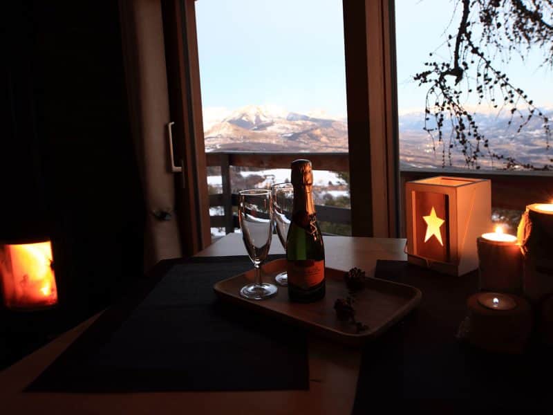 Cabane en bois avec vue sur les montagnes, champagne et bougies créent une ambiance romantique.