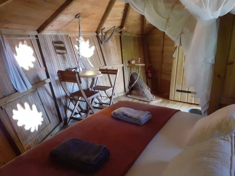 Cabane en bois avec lit douillet et décoration chaleureuse. Ambiance naturelle et cosy.