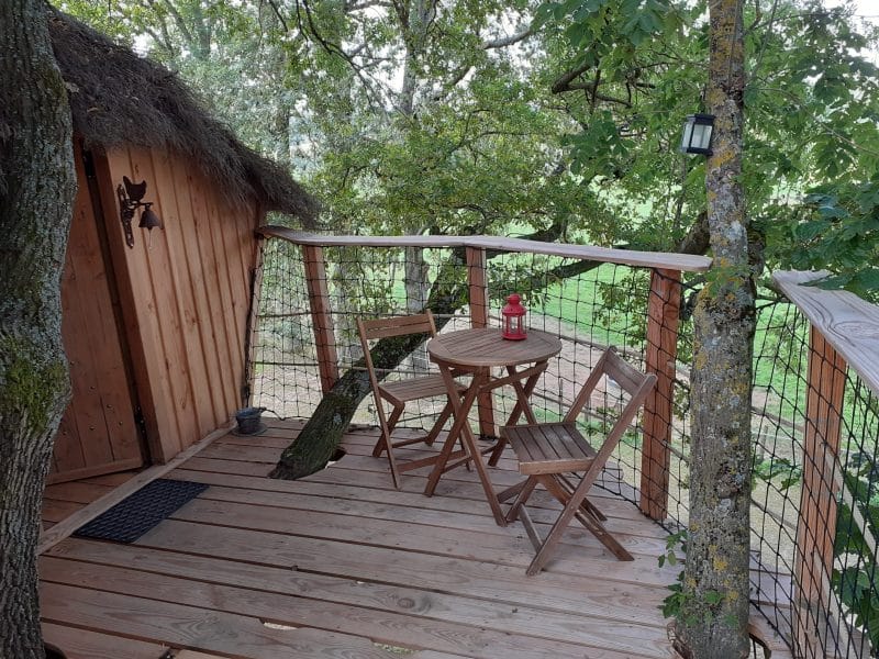 Cabane dans les arbres avec terrasse en bois et vue sur la nature environnante.