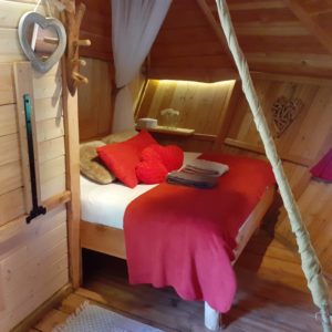 Cabane en bois cosy en Bourgogne, lit douillet avec décor chaleureux et rouge.