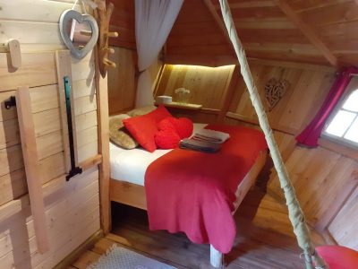 Cabane en bois cosy en Bourgogne, lit douillet avec décor chaleureux et rouge.