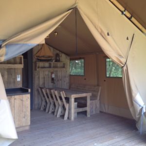 Tente safari spacieuse avec mobilier en bois et vue sur la nature.