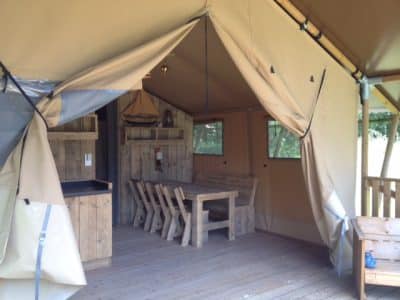 Tente safari spacieuse avec mobilier en bois et vue sur la nature.