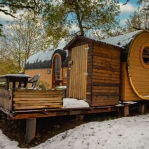 Hébergement insolite en forme de cabane en bois, entouré de neige et darbres.