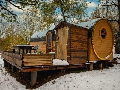 Hébergement insolite en forme de cabane en bois, entouré de neige et darbres.