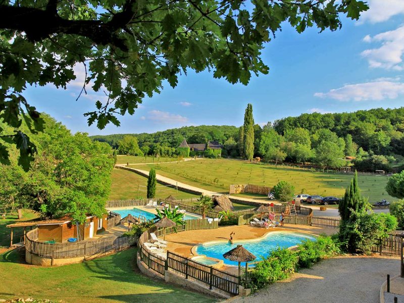 Camping avec piscine entourée de verdure et vue sur la nature environnante.