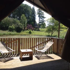 Tente safari avec terrasse en bois, vue sur un paysage verdoyant et paisible.
