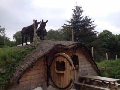 Hébergement insolite en forme de hobbit avec un toit en herbe et des ânes à proximité.