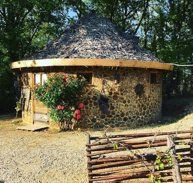 Hébergement en cabane ronde en pierre, toit de chaume, entourée de verdure.