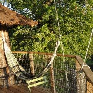 Cabane perchée avec hamac, entourée de verdure luxuriante au Centre.