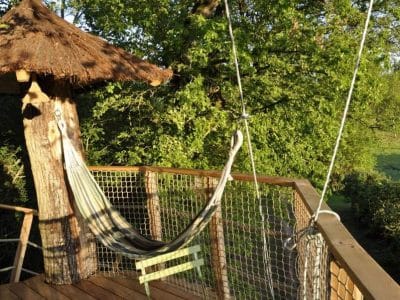 Cabane perchée avec hamac, entourée de verdure luxuriante au Centre.