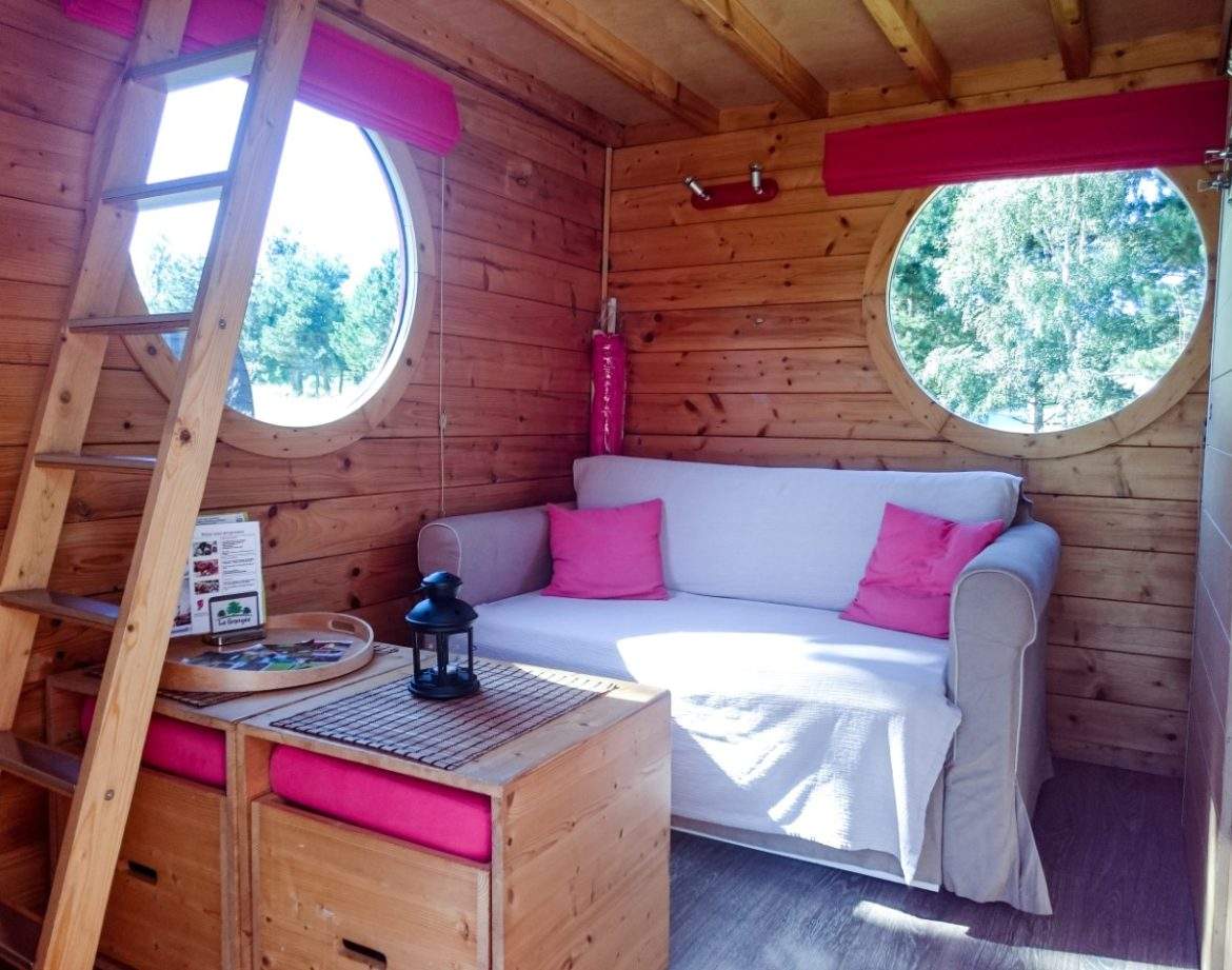 Cabane en bois avec fenêtres rondes et canapé confortable, idéale pour un séjour unique.