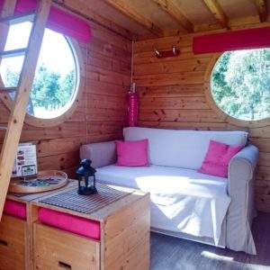 Cabane en bois avec fenêtres rondes et canapé confortable, idéale pour un séjour unique.