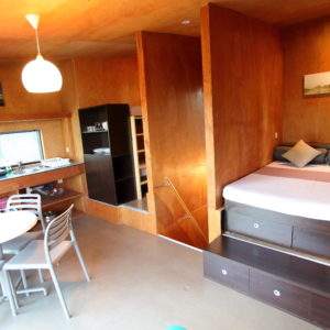 Hébergement insolite en Basse-Normandie : intérieur en bois avec lit confortable et coin cuisine.