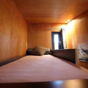 Cabane en bois cosy avec lit simple et fenêtre laissant entrer la lumière.