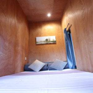 Cabane en bois à Basse-Normandie, intérieur chaleureux avec lit et coussins confortables.