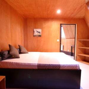 Chambre en bois moderne à Basse-Normandie, avec lit confortable et lumière naturelle.