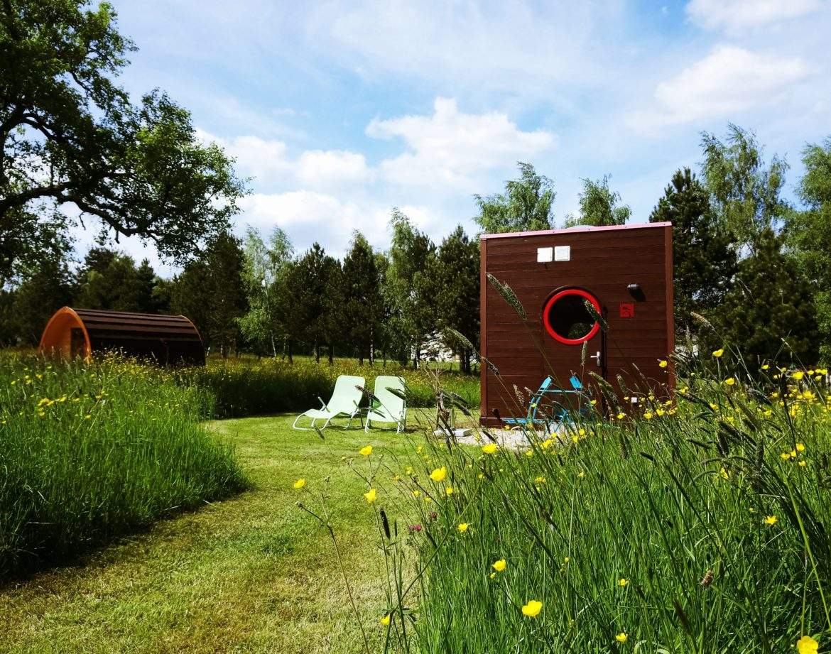 Hébergement insolite en forme de cube, entouré de fleurs sauvages et de chaises longues.