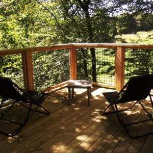 Cabane perchée en Basse-Normandie, avec terrasse en bois et chaises confortables.