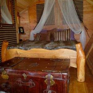 Chalet en bois avec lit douillet et coffre ancien, ambiance chaleureuse et rustique.