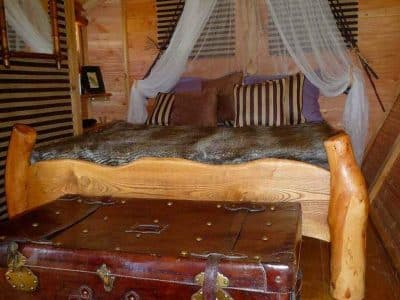 Chalet en bois avec lit douillet et coffre ancien, ambiance chaleureuse et rustique.
