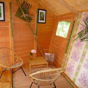 Hébergement insolite en cabane bois, décoré avec des plantes et des fauteuils en rotin.