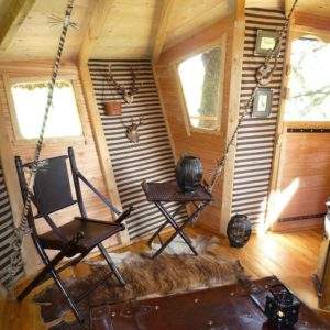 Hébergement insolite en cabane avec chaises suspendues et décor en bois chaleureux.