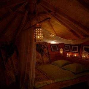 Cabane cosy avec lit douillet, éclairage chaleureux et décor en bois.