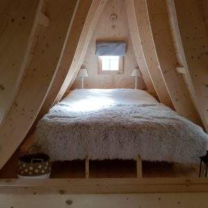 Chalet en bois dans les arbres, lit douillet avec couverture en fausse fourrure.