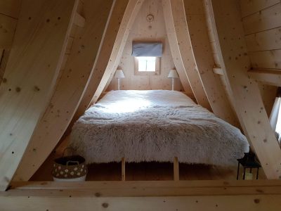Chalet en bois dans les arbres, lit douillet avec couverture en fausse fourrure.