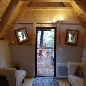 Cabane en bois avec intérieur chaleureux et vue sur la forêt depuis la porte.