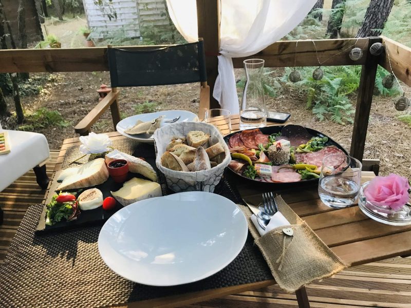 Terrasse dun gîte avec un repas gourmet, entourée de verdure apaisante.