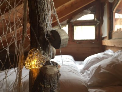 Cabane en bois avec éclairage doux et literie confortable, ambiance chaleureuse.