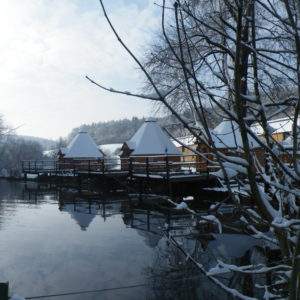 Hébergement insolite en cabanes sur pilotis, entouré de neige et deau paisible.