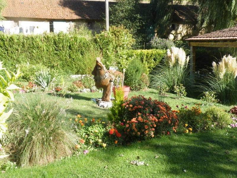 Gîte charmant avec jardin fleuri et sculpture en bois au centre.