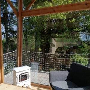 Cabane en bois avec vue sur la nature, fauteuil confortable et poêle à bois.