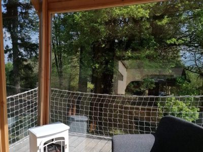 Cabane en bois avec vue sur la nature, fauteuil confortable et poêle à bois.
