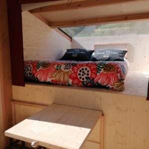 Cabane en bois avec lit coloré et table en bois, idéale pour un séjour insolite.