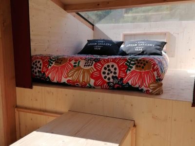 Cabane en bois avec lit coloré et table en bois, idéale pour un séjour insolite.