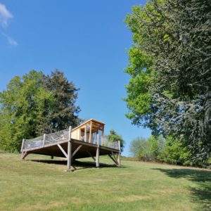 Cabane sur pilotis en pleine nature, entourée darbres verdoyants et ciel bleu.