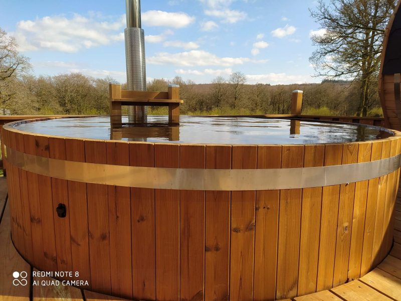 Hébergement insolite avec un jacuzzi en bois, entouré de nature verdoyante.