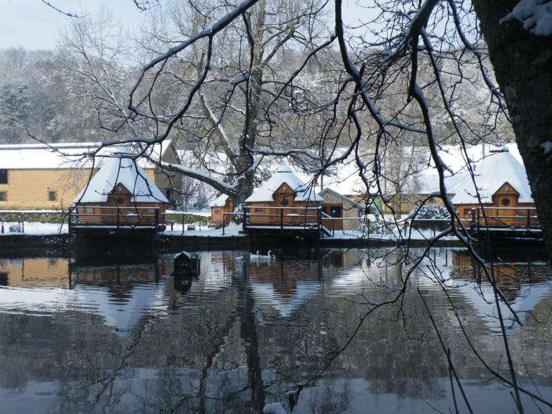 Cabines en bois au bord dun lac, entourées de neige et de paysages paisibles.