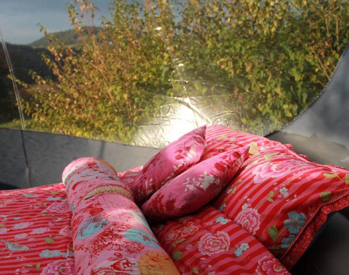 Tente transparente avec literie colorée, vue sur la nature en Auvergne-Rhône-Alpes.