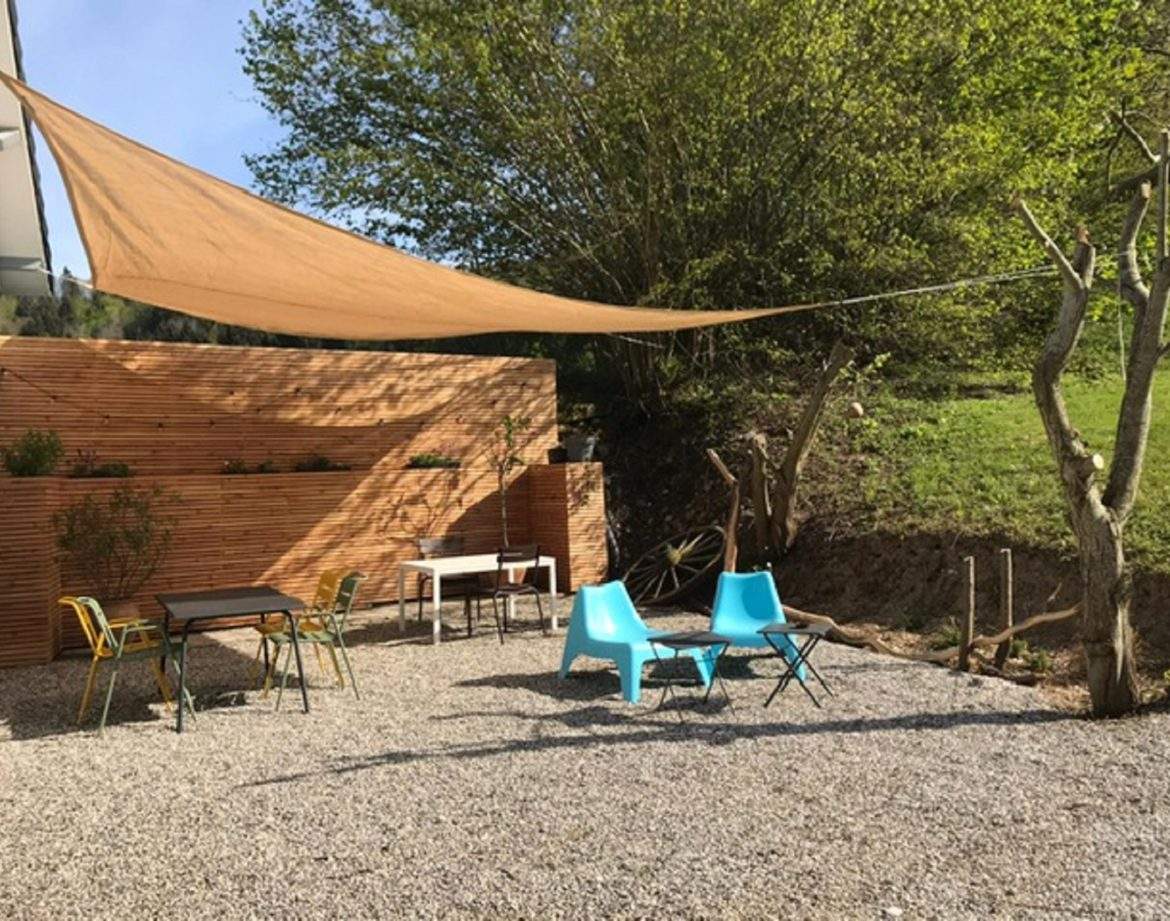 Espace extérieur dun hébergement insolite avec chaises colorées et toile dombrage.