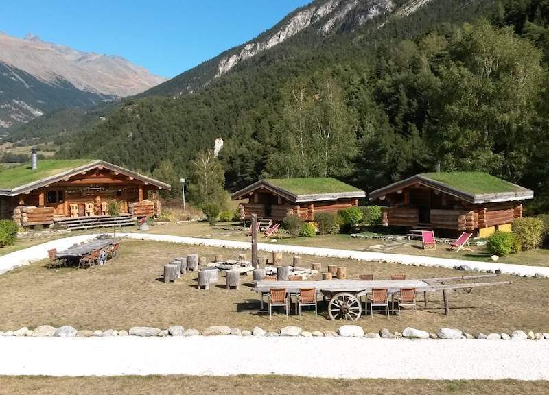 Chalets en bois avec toits végétalisés, entourés de montagnes verdoyantes.